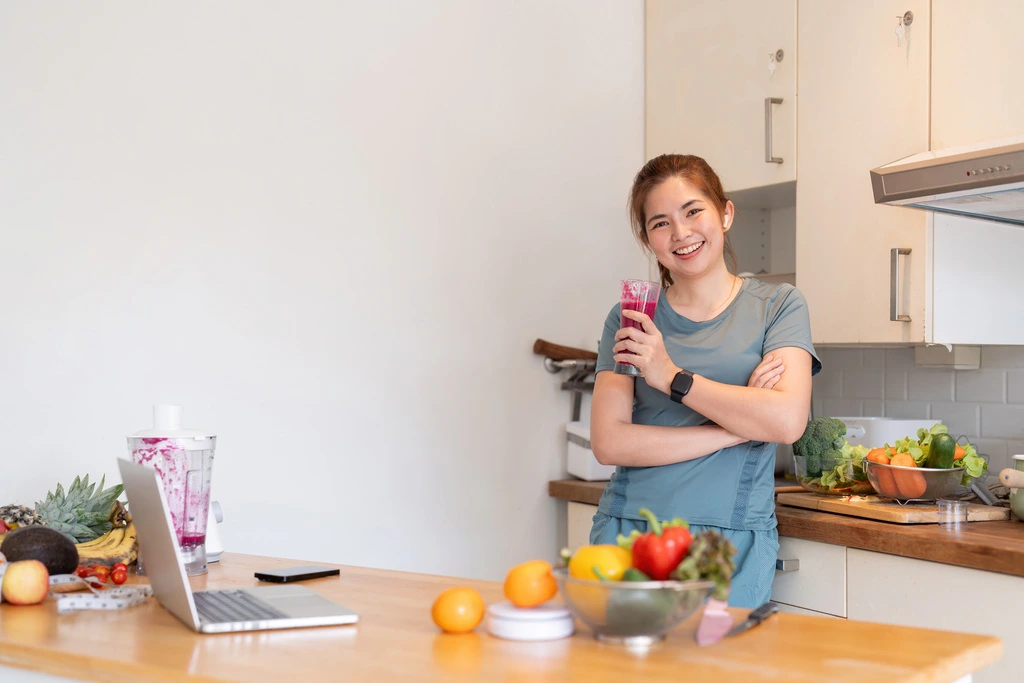 Maya Thompson of Bring Dish standing confidently in her kitchen with a fresh smoothie and ingredients on the counter.
