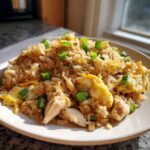 A close-up of a serving of homemade chicken fried rice, featuring rice, chunks of chicken, scrambled egg, and green onions.