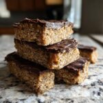 Close-up of a stack of homemade protein bars featuring an oat base, caramel layer, and rich chocolate topping.