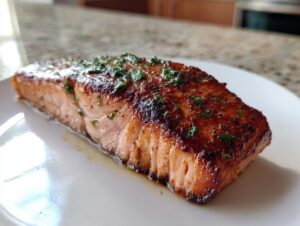 Close-up of a beautifully seasoned and cooked air fryer salmon fillet resting on a white plate.