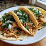 Close-up of three soft corn tortillas filled with shredded seasoned chicken, topped generously with diced white onion and fresh cilantro for amazing chicken tacos.