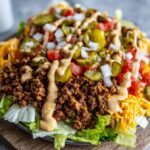 Close-up of a delicious cheeseburger bowl piled high with seasoned ground beef, lettuce, cheese, pickles, and a creamy sauce.