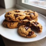 A stack of freshly baked chewy chocolate chip cookies with melted chocolate chunks on a white plate.