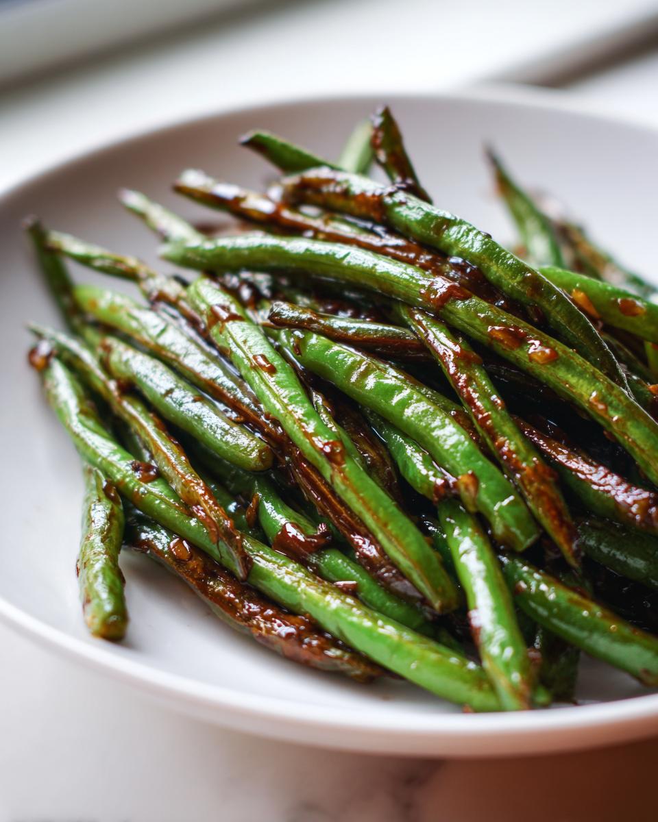 Close-up of vibrant green beans coated in a glossy, dark garlic sauce, ready to serve.