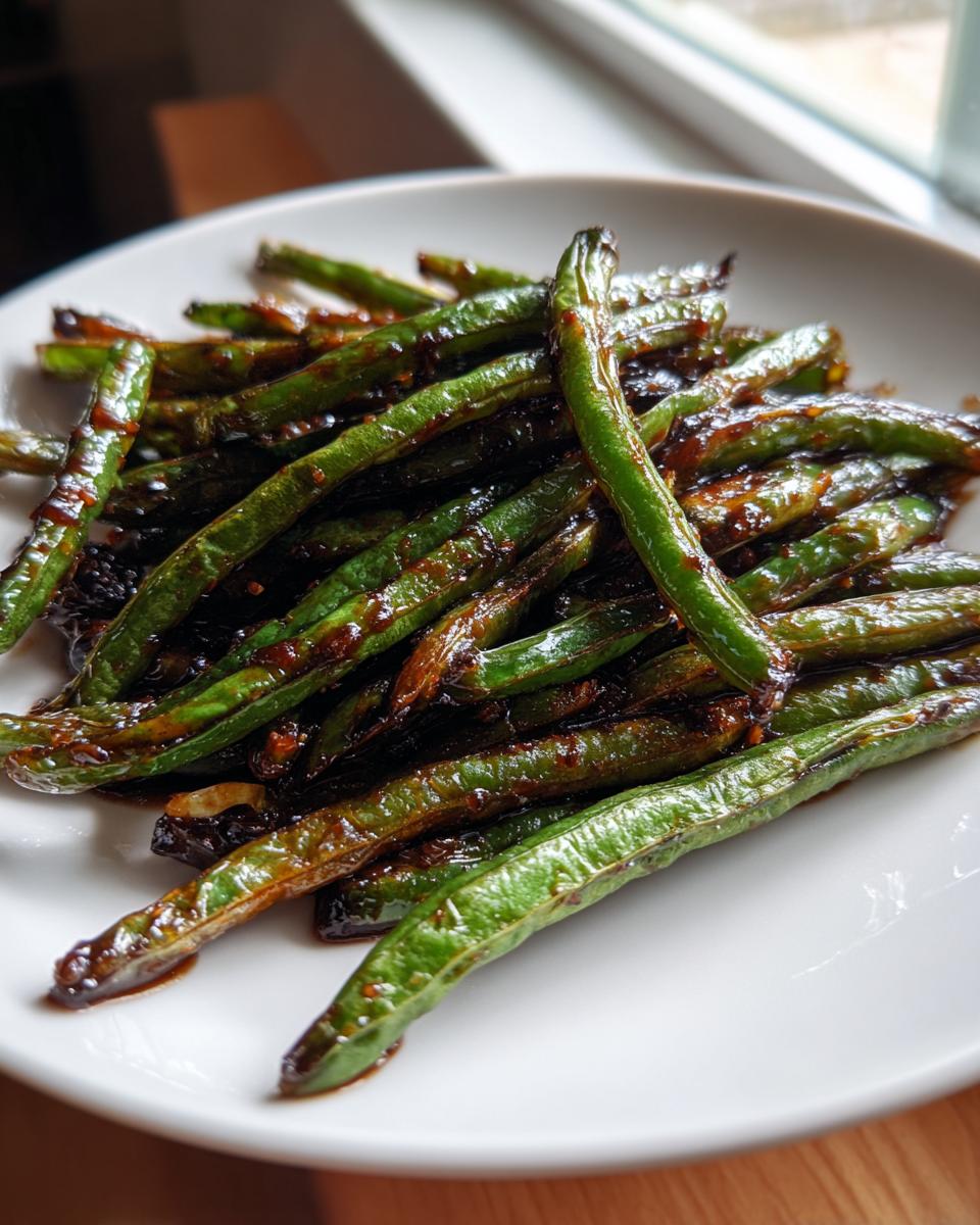 A close-up of vibrant, blistered chinese green beans with garlic sauce piled high on a white plate.