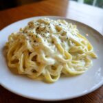 Close-up of fettuccine pasta generously coated in creamy Olive Garden Alfredo Sauce and topped with herbs.