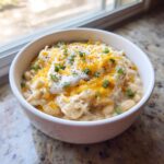 A close-up of a white bowl filled with creamy crockpot white chicken chili, topped with shredded cheese, sour cream, and chives.