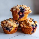 A stack of three golden brown blueberry muffins topped with a generous brown sugar crumble.