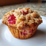 A close-up of a single, freshly baked strawberry muffins topped with a golden brown streusel crumb topping.