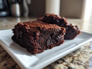 Close-up of two fudgy date brownies with shiny, crackled tops served on a white rectangular plate.