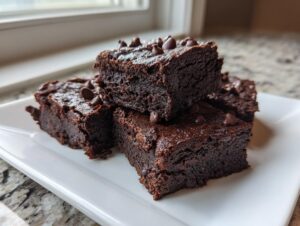 A stack of four fudgy sweet potato brownies topped with chocolate chips, resting on a white rectangular plate.