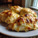 Four golden-brown, cheesy servings of Garlic parmesan chicken bake on a white plate, fresh from the oven.