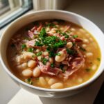 Close-up of a white bowl filled with rich Ham and Bean Soup, topped with shredded ham and fresh parsley.