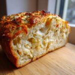 A close-up of the interior crumb structure of Italian herb and cheese bread, showing melted cheese pockets and rosemary topping.