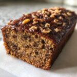 Close-up of a moist date nut bread loaf, featuring a shiny glaze and chopped walnuts on top.