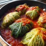 Close-up of several homemade cabbage rolls simmering in a rich tomato sauce in a black pot.
