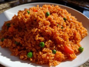 A close-up of vibrant, orange-red Spanish rice mixed with bright green peas and diced carrots on a white plate.