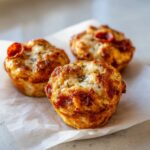 Close-up of three freshly baked pizza muffins topped with melted cheese, herbs, and small pepperoni slices.
