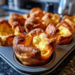 Close-up of golden brown, puffed Yorkshire pudding baked in a dark muffin tin, showing the impressive rise.