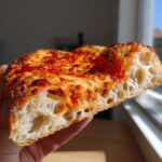 Close-up of a slice of pizza showing the airy, open crumb structure made from sourdough discard pizza dough.