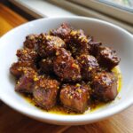 Close-up of tender crockpot steak bites coated in a rich, glossy sauce and sprinkled with chili flakes.