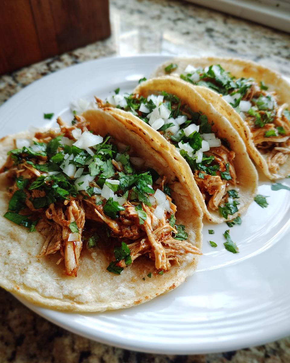 Three soft corn tortillas filled with shredded seasoned chicken, topped with fresh diced white onion and cilantro for amazing chicken tacos.