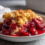 Close-up of a warm serving of 3 ingredient cherry dump cake with a golden, crumbly topping and rich, bright red cherry filling.
