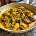 Close-up of tender pieces of coconut chicken simmering in a rich, yellow, creamy sauce and garnished with fresh cilantro.