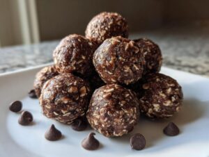 A stack of homemade chocolate protein balls made with oats, garnished with scattered chocolate chips on a white plate.