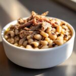 Close-up of a white bowl filled with creamy black eyed peas topped with shredded smoked meat.
