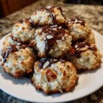A stack of freshly baked almond joy cookies drizzled with melted chocolate and topped with sliced almonds.