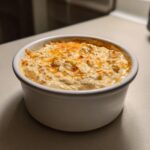 A close-up of a freshly baked, creamy beer cheese dip topped with melted orange cheese, served in a white round baking dish.
