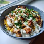 A close-up of a delicious chicken rice bowl topped with grilled chicken, corn, creamy sauce, and fresh parsley.