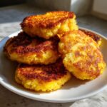 A stack of perfectly golden brown, crispy fried cornbread patties resting on a white plate.