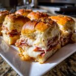 Close-up of cheesy, meaty grinder sliders with melted provolone on a white platter.