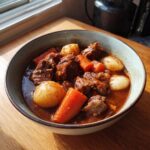 A close-up of a rustic bowl filled with tender chunks of pork stew, carrots, and potatoes in a rich, dark gravy.