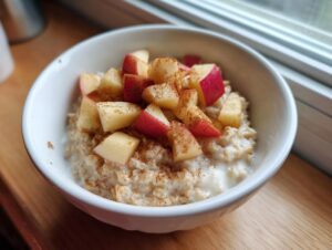 A white bowl filled with creamy apple cinnamon oatmeal, topped with diced red apples and a dusting of cinnamon.