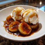 Two scoops of vanilla ice cream melting over caramelized bananas in rich sauce, classic Bananas Foster.
