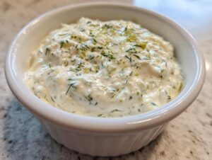 Close-up of creamy homemade tartar sauce topped with fresh dill and zest in a small white bowl.