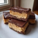 Close-up of stacked buckeye fudge bars showing thick peanut butter filling and chocolate topping on a white plate.