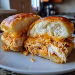 Close-up of a delicious buffalo chicken sliders cut in half, showing shredded chicken, melted cheddar cheese, and soft rolls.