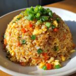 A mound of golden cauliflower fried rice mixed with scrambled egg and carrots, topped with fresh green onions.