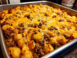 Close-up of baked Cheesy Taco Potatoes casserole topped with melted cheddar cheese and seasoned ground beef in a metal baking dish.