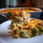 A spoonful of creamy chicken cauliflower rice casserole topped with melted, browned cheese being lifted from a serving on a white plate.