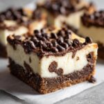 A rich, thick slice of chocolate chip cheesecake bar featuring a brownie base, creamy filling, and topped with melted chocolate and chips.