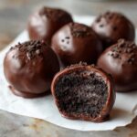 Close-up of several chocolate-coated Oreo balls, one of which has a bite taken out revealing the dark, dense interior.