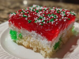 Close-up of a festive slice of Christmas poke cake featuring layers of white cake, green jello, white topping, and red jello with sprinkles.