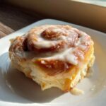 A close-up of a single, freshly baked cinnamon roll with thick white icing, perfect for cinnamon rolls with heavy cream recipes.