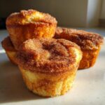 Four golden french toast muffins heavily coated in sparkling cinnamon sugar, illuminated by sunlight.