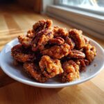 A mound of glistening, candied cinnamon sugar pecans piled high on a small white plate, catching the sunlight.